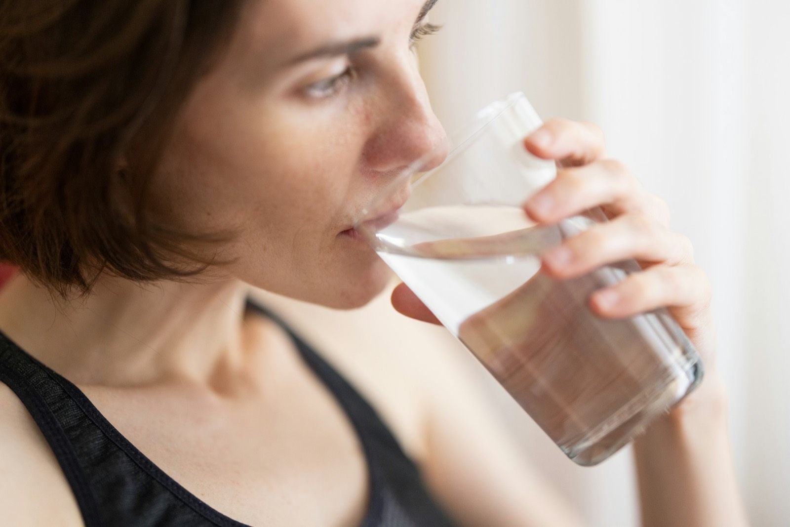 A woman with short dark hair drinking from a glass of water