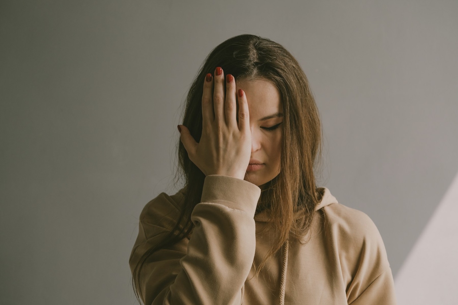 A young woman with her eyes closed, resting her forehead against her hand