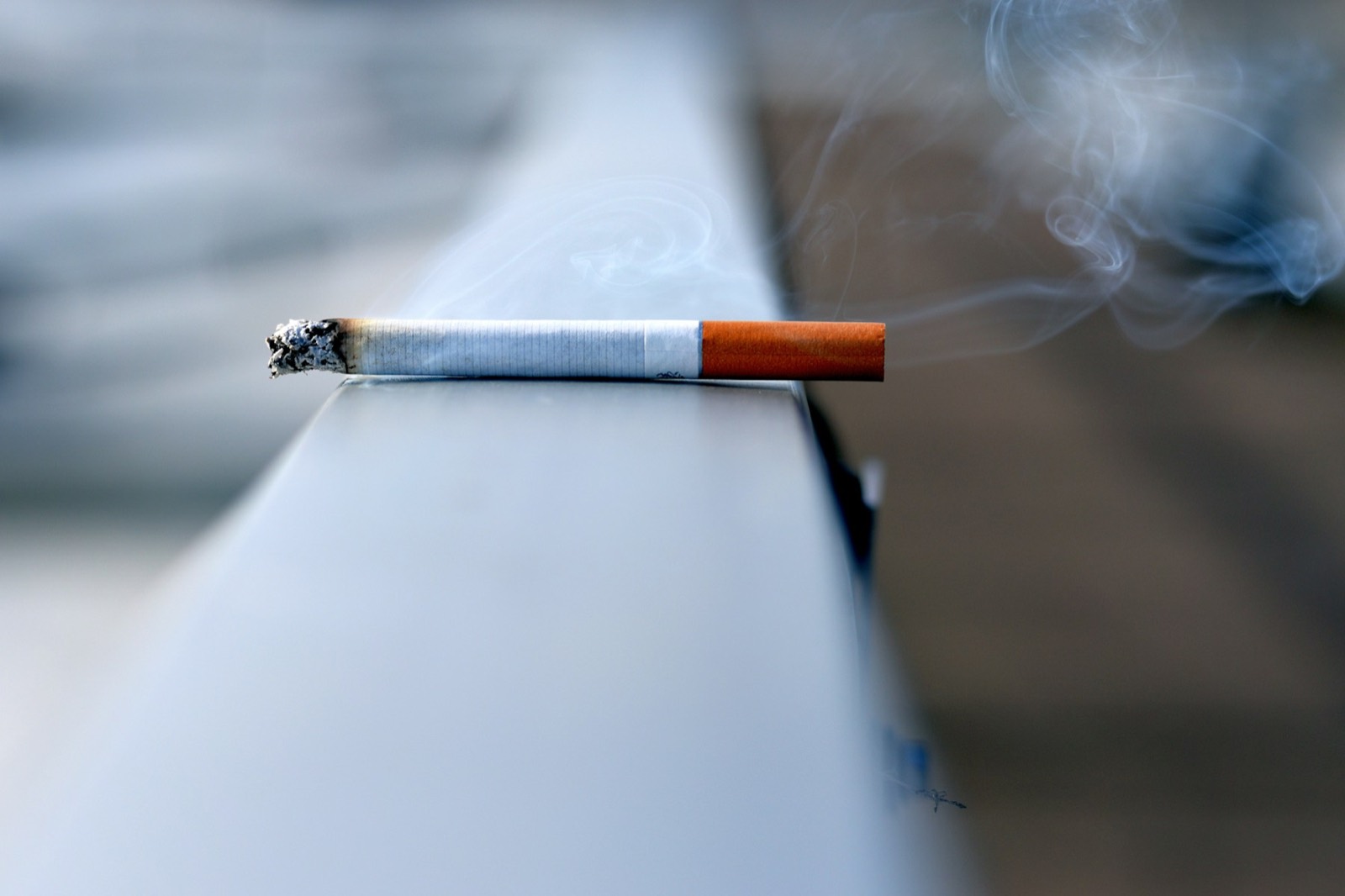 A lit cigarette resting on a concrete ledge, out of focus behind it