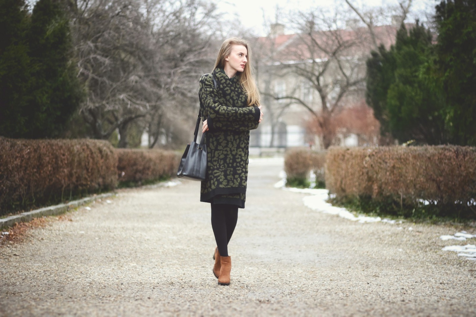 A woman in a long coat walking along a park path lined with bare trees