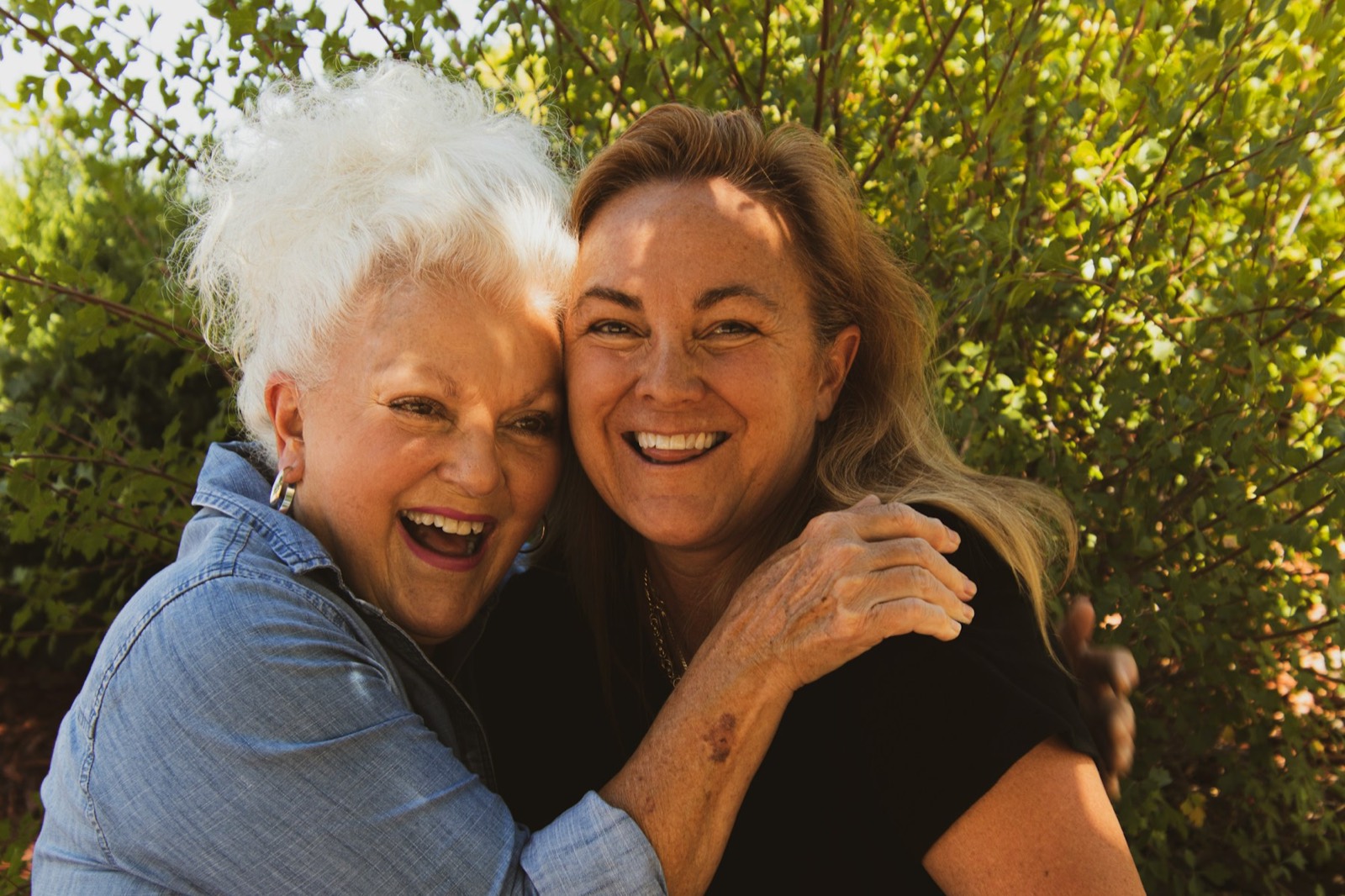 An older woman and her grown daughter hugging and laughing outdoors
